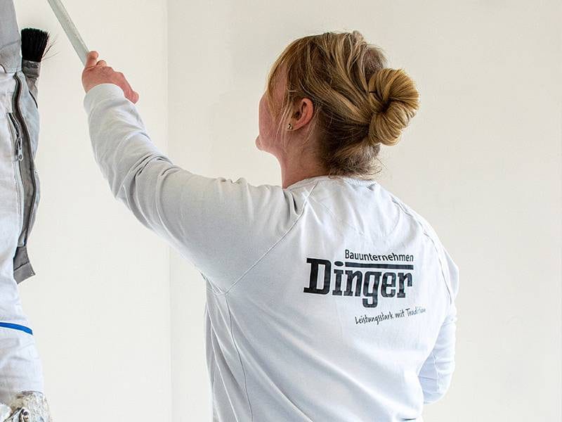 Mitarbeiterin im Dinger-Arbeitsshirt beim Anstrich einer Wandfläche