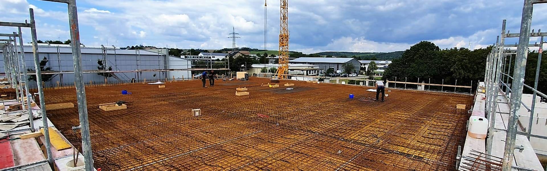 Bewehrung einer Bodenplatte auf einer Baustelle, dahinter Gerüst und Baukran