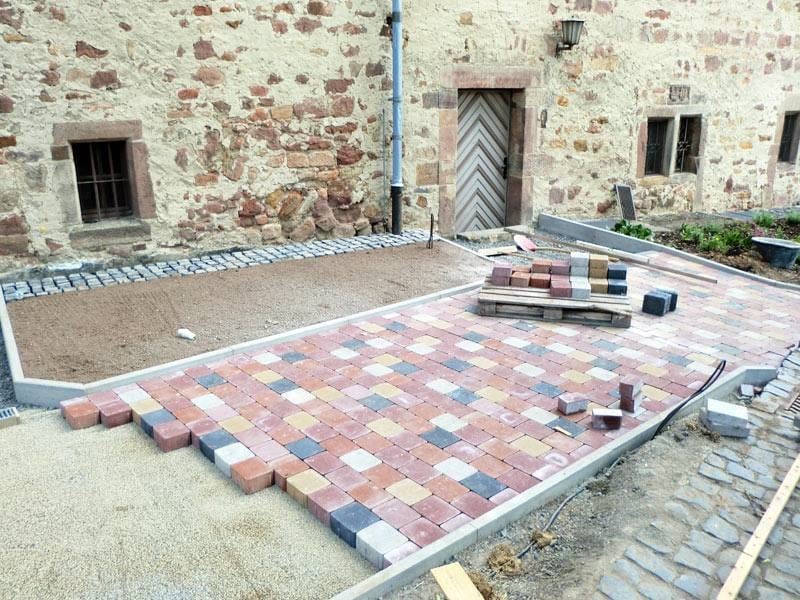 Hoffläche im Bau: verlegtes Pflaster, ausgelegte Beton- und Natursteine vor einer Natursteinmauer