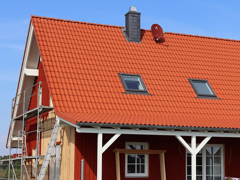 Rote Ziegeleindeckung mit zwei Dachfenstern über einer roten Holzfassade, Gerüst am Giebel