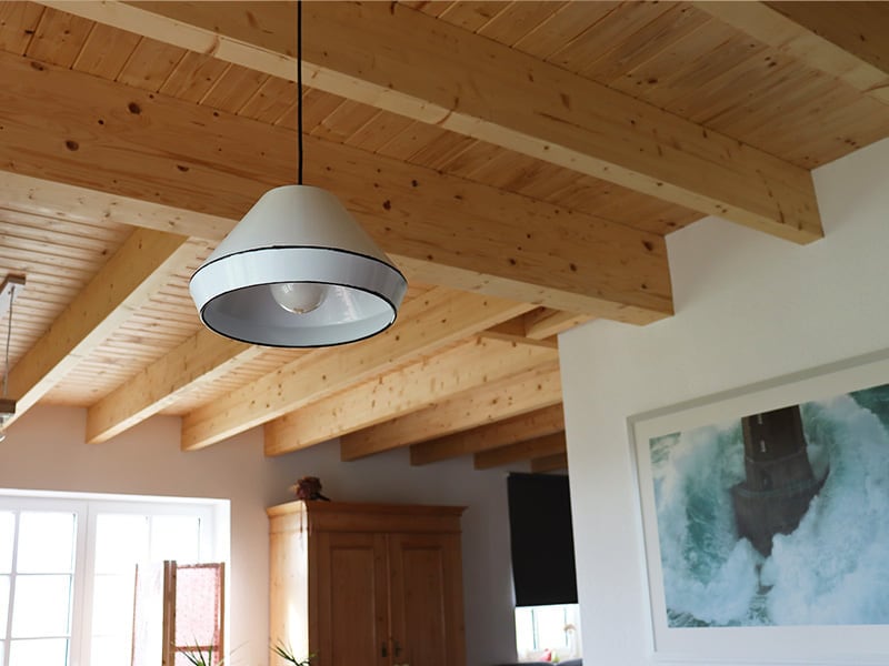 Wohnraum mit sichtbarer Holzbalkendecke, Pendelleuchte und hell verputzten Wänden
