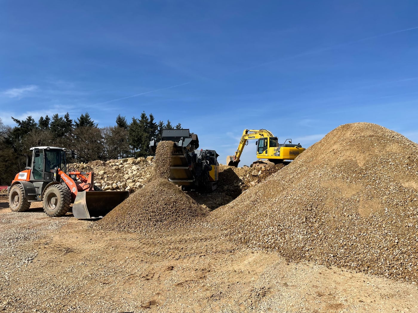Radlader und Bagger vor einer Halde aufbereiteten Materials auf dem Recyclinghof