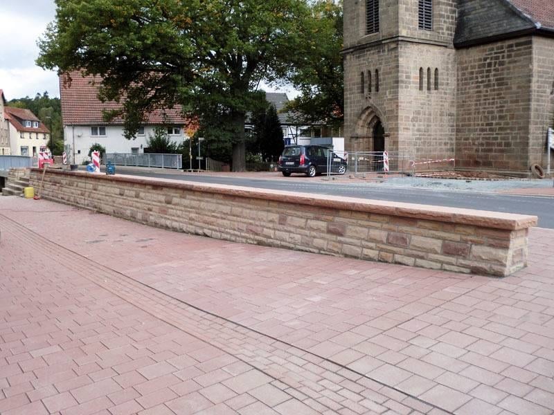 Instand gesetzte Natursteinmauer mit gepflasterter Platzfläche vor einem historischen Gebäude