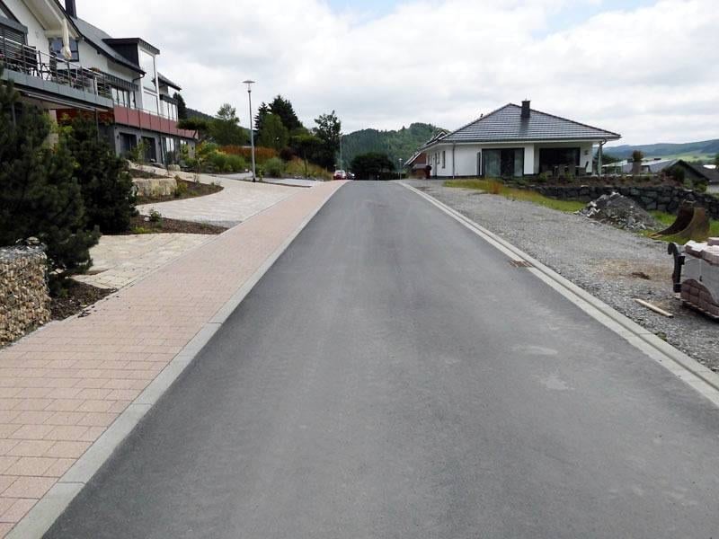 Fertige Asphaltfläche mit Bordstein und angrenzendem Schotterstreifen