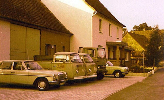 Ein Personenwagen und zwei Kleintransporter mit Firmenaufschrift vor einem Hofgebäude