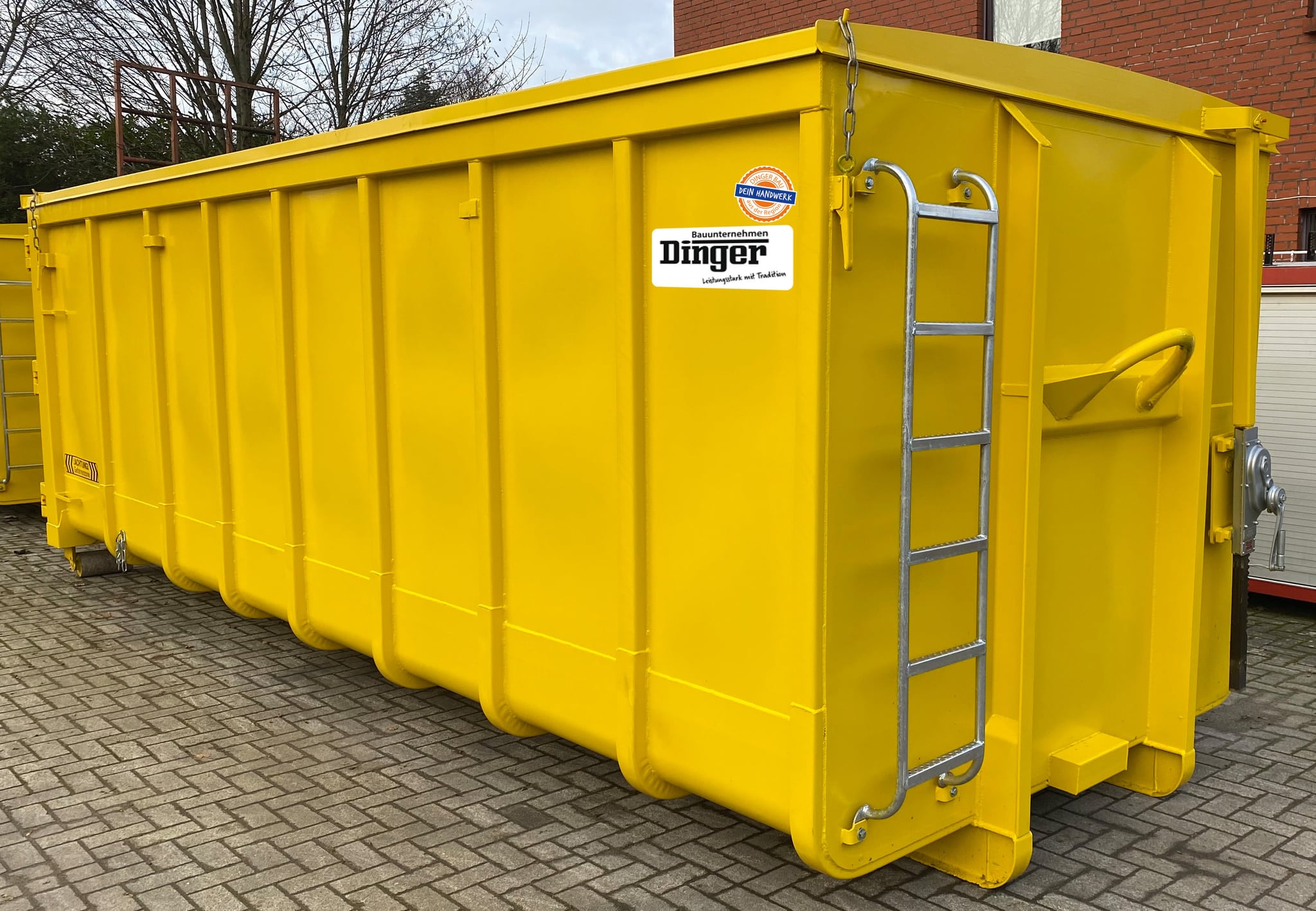 Gelber Abrollcontainer von Dinger Bauunternehmen mit Einstiegsleiter auf gepflastertem Hof