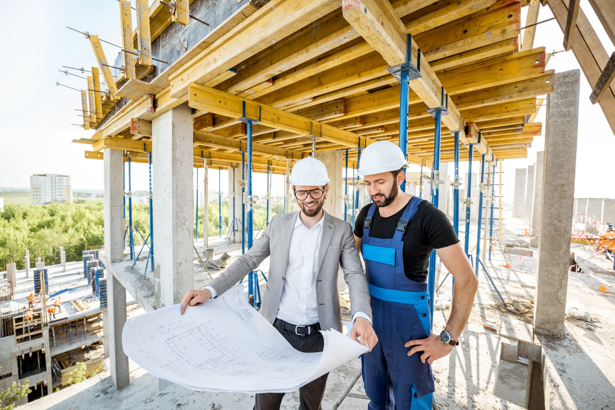 Zwei Männer mit Schutzhelmen besprechen einen Bauplan auf einer Baustelle