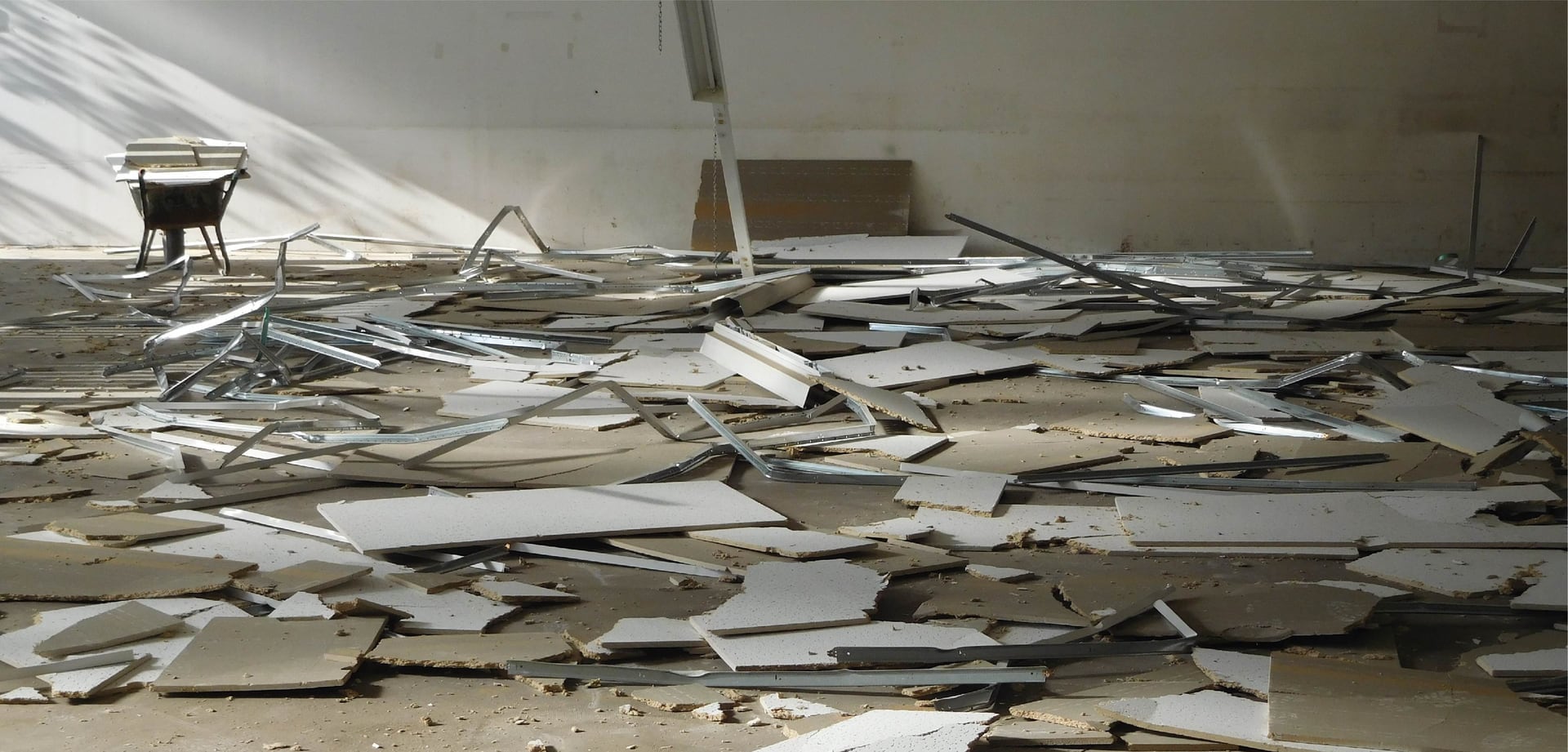 Innenraum im Rückbau – abgenommene Deckenplatten und Metallprofile auf dem Boden, Tageslicht von der Seite